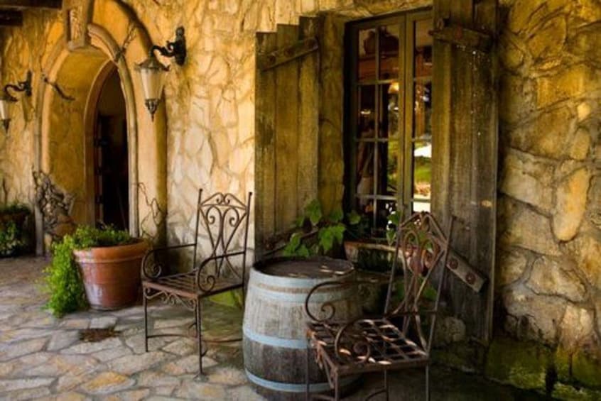 A stone building with a rustic outdoor seating area, including metal chairs and a barrel. 3