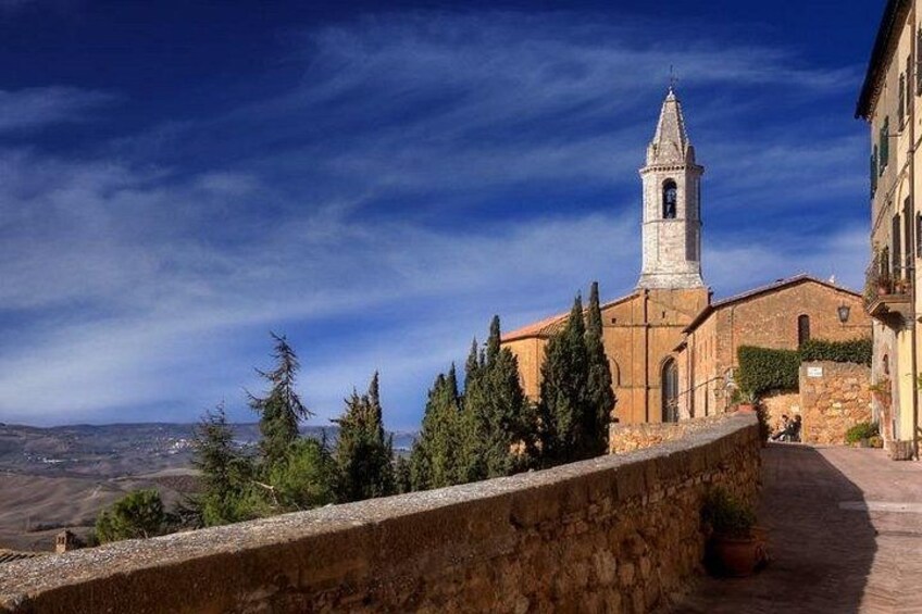 Un muro de piedra, una iglesia con campanario y un cielo azul despejado. 3