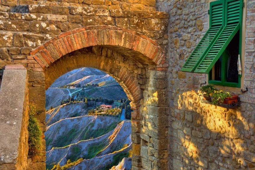 A stone archway with a view of a valley, a building with green shutters, and a stone wall. 3