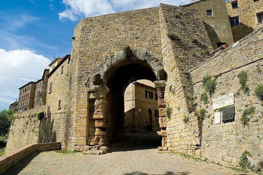A stone archway leading into a courtyard with buildings in the background. 4