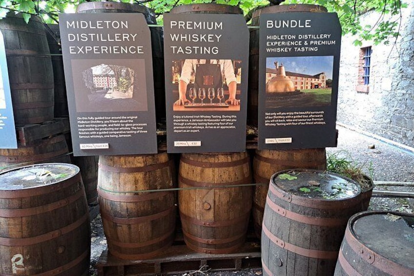 Tres barriles de madera con letreros que anuncian una experiencia en una destilería, degustación de whisky premium y una oferta especial. 2