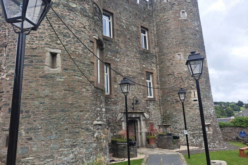 A historic stone building with a tower, a paved entrance, and traditional street lamps. 5