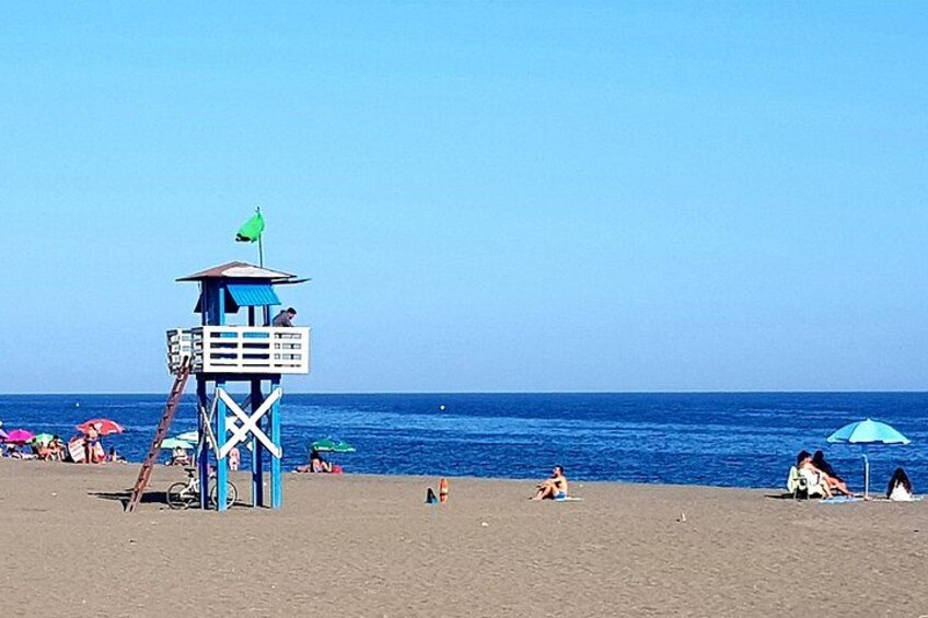 A beach with a lifeguard tower, umbrellas, and people relaxing on the sand. 5