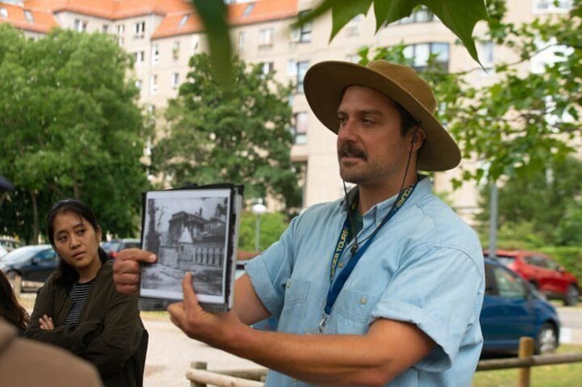 A man in a hat gesturing, a woman holding a photo, and a building in the background. 3