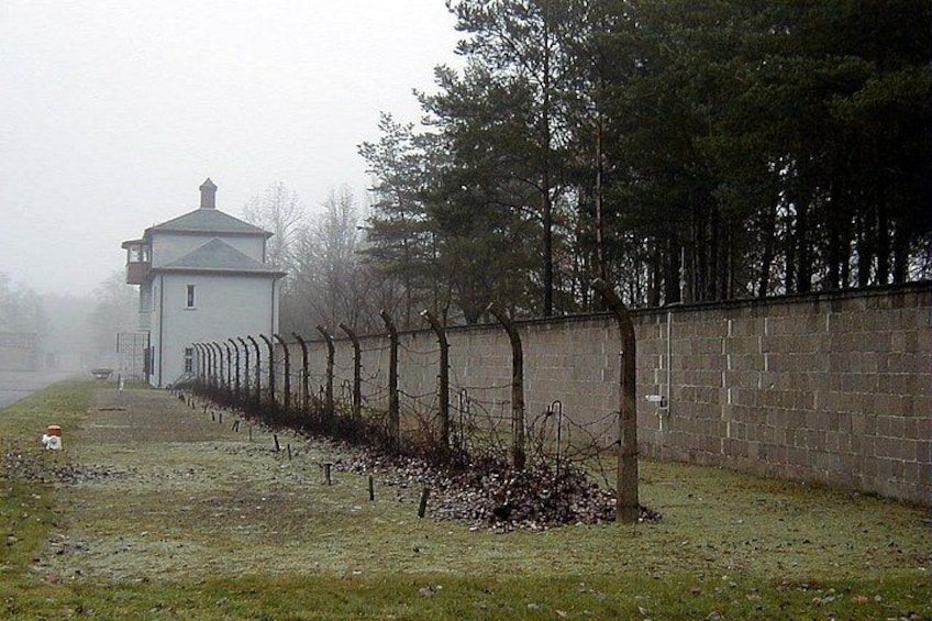 A fenced area with a watchtower, a barbed wire fence, and a grassy field. 4