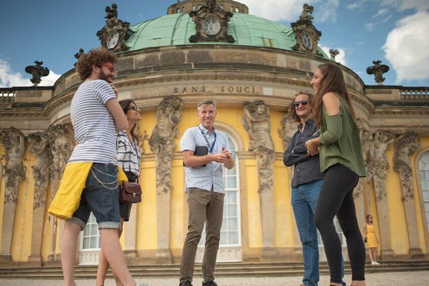 A group of people standing in front of a historic building with ornate architecture and a green dome. 1