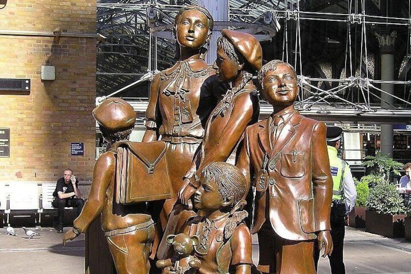 En bronze statue af en familie med et barn foran en murstensbygning med stillads. 2