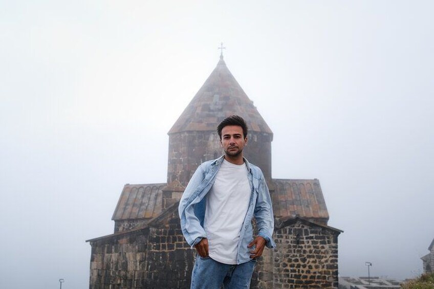 A person standing in front of a stone building with a pointed roof. 2