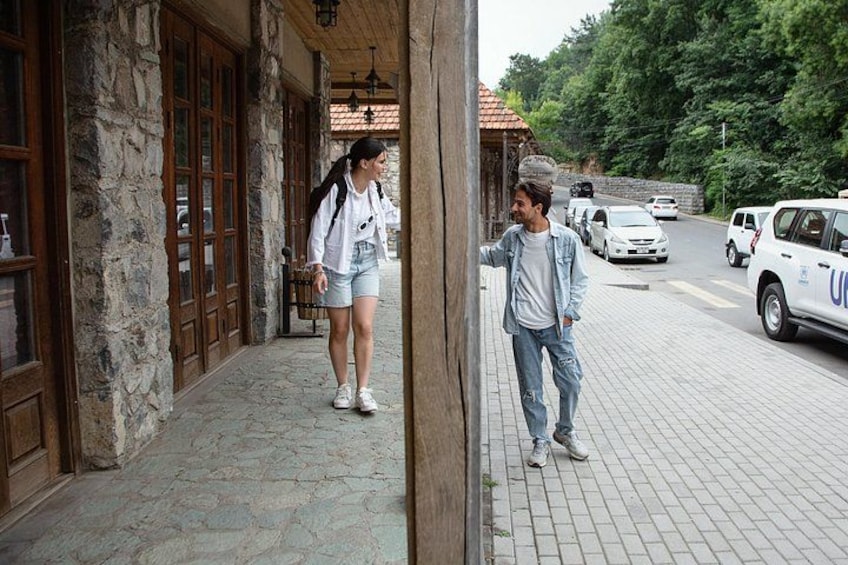 A stone building with wooden doors, a paved sidewalk, and a parked white car with blue lettering. 4