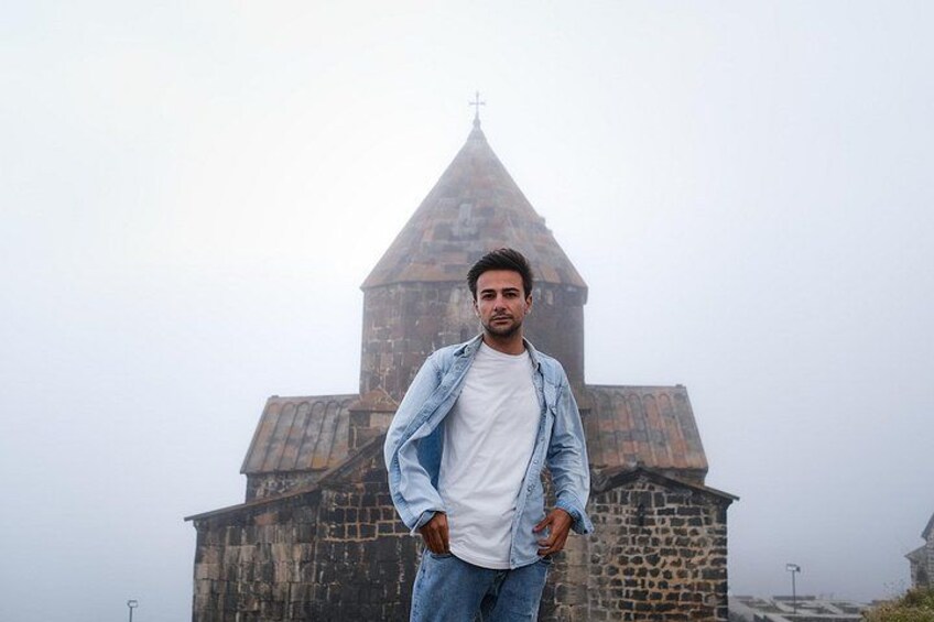 A person standing in front of a historic stone building with a pointed roof and a cross on top. 5