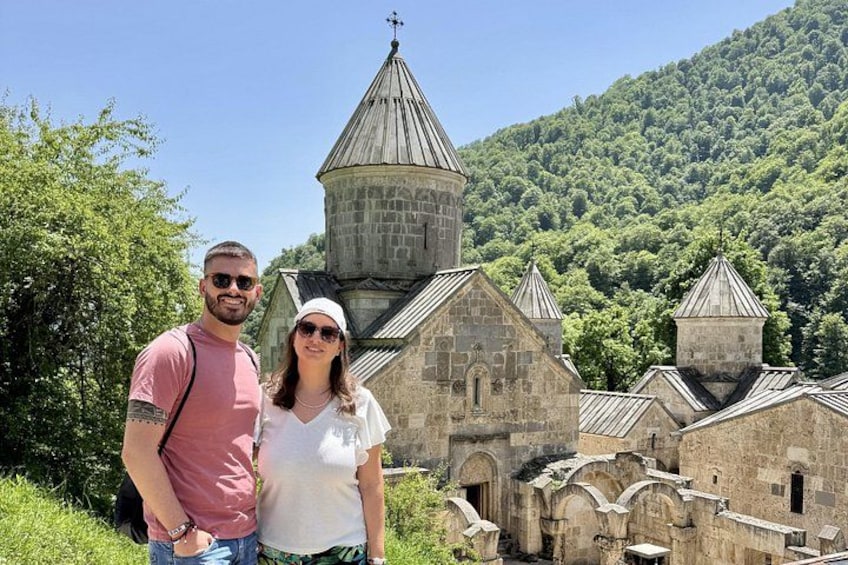 A historic church with a bell tower and a forested hillside in the background. 1