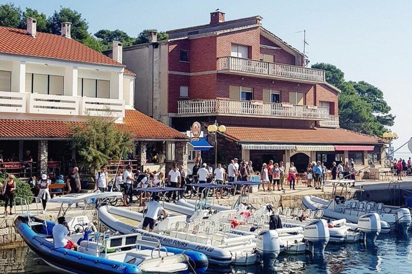 Een jachthaven met aangemeerde boten, mensen die lopen, en gebouwen met rode pannendaken. 5