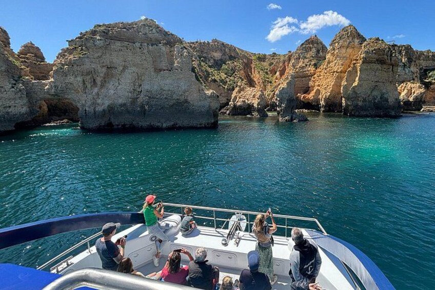 A boat with people on a clear day, surrounded by rocky cliffs and turquoise water. 1