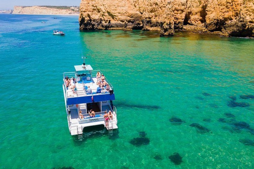 A boat with passengers on a clear turquoise sea, rocky cliffs in the background, and another boat in the distance. 2
