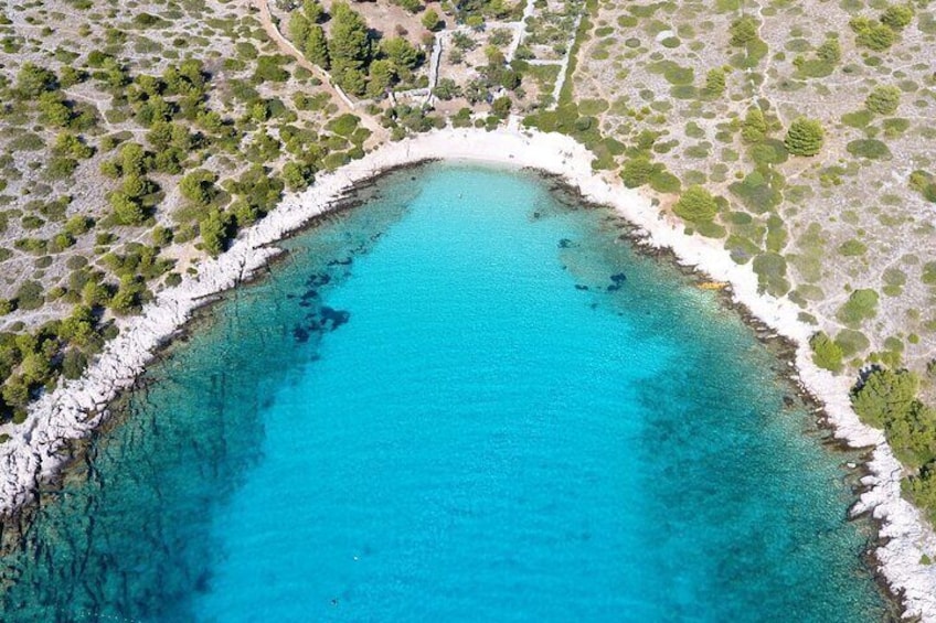 An aerial view of a turquoise bay with a white sandy beach and scattered vegetation. 1