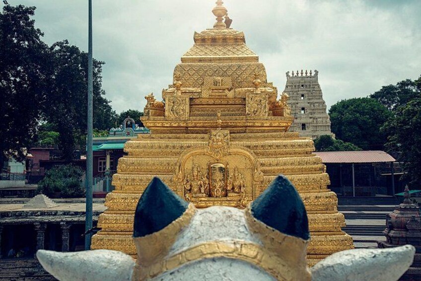 Ein goldener Tempel mit aufwendigen Schnitzereien, eine weiße Elefantenstatue im Vordergrund und ein traditionelles Gebäude im Hintergrund. 1