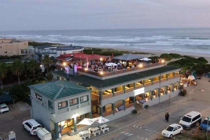 A coastal building with a balcony overlooking the beach, a parking area, and a road leading to the beach. 2