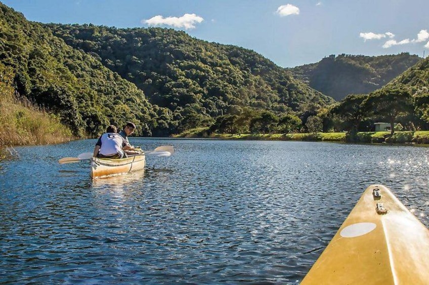 Two people in a canoe on a calm river, surrounded by lush green hills. 3