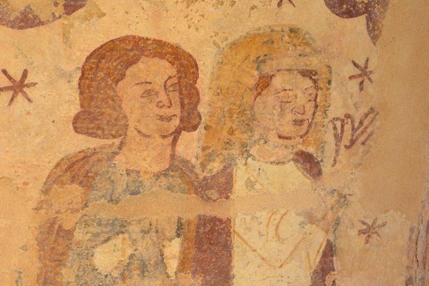 Un fresco descolorido con dos figuras, una con un halo, y elementos decorativos como estrellas y cruces. 1