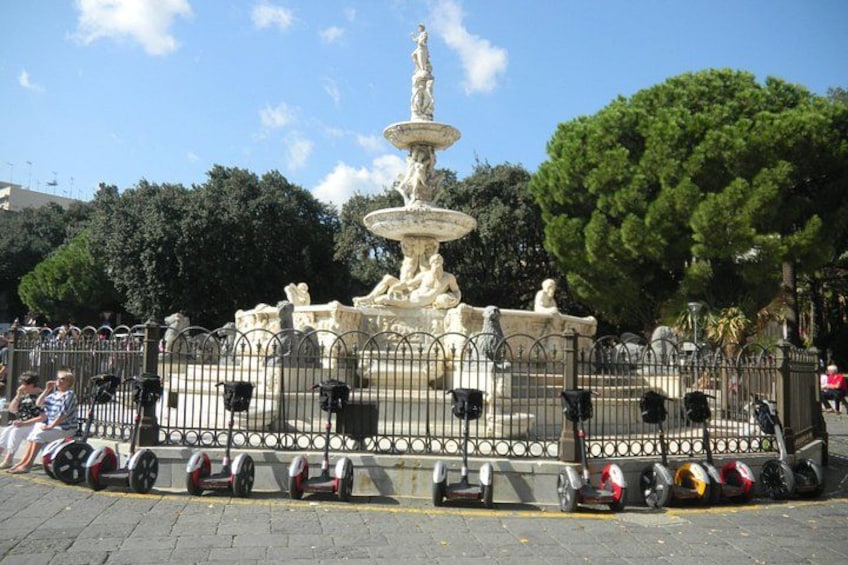 Una fuente con estatuas, rodeada por una valla, y varios scooters estacionados. 4