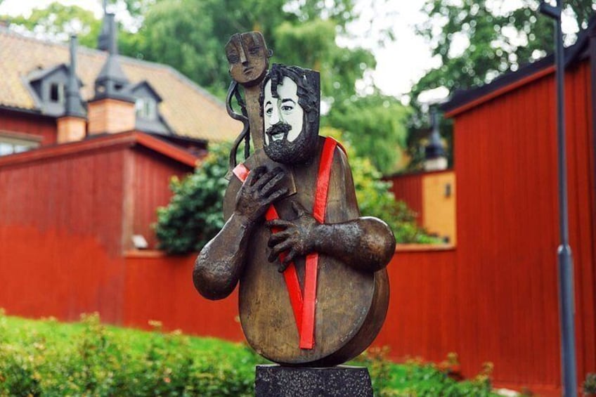 Una scultura raffigura un uomo che tiene un nastro rosso, sullo sfondo di un edificio rosso e vegetazione. 2