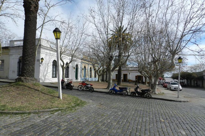 A cobblestone street with parked scooters and a white building with arched windows. 3
