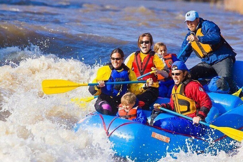A group of people in a blue raft navigating through white water rapids. 2