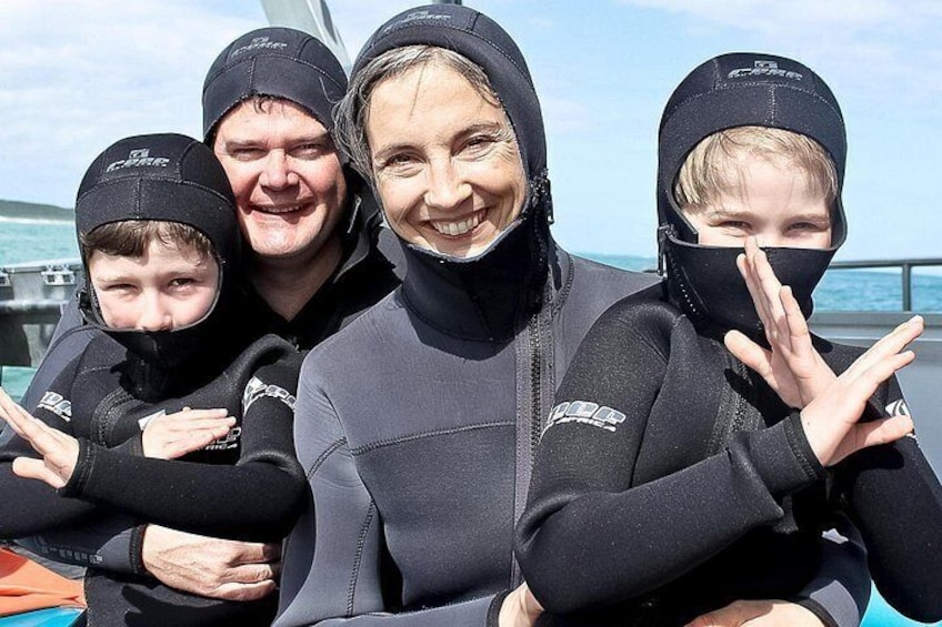A group of people wearing wetsuits and scuba diving gear, standing on a boat with the ocean in the background. 5