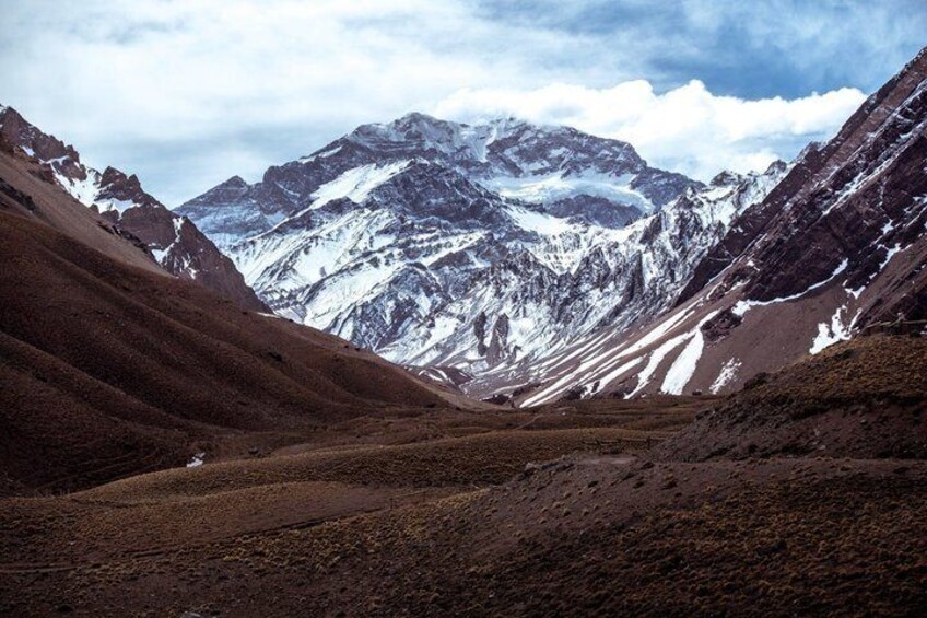 A mountainous landscape with a valley, snow-capped peaks, and a clear sky. 1