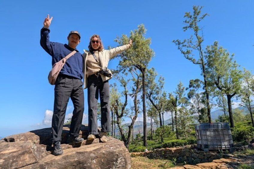 Two people standing on a rock with a clear sky and trees in the background. 5