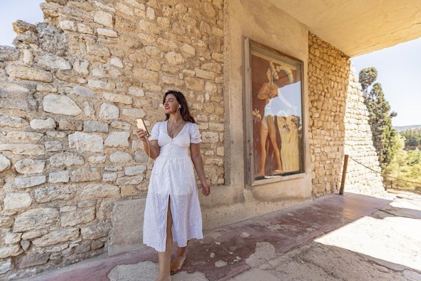 A woman in a white dress standing in front of a stone building with a large window. 3