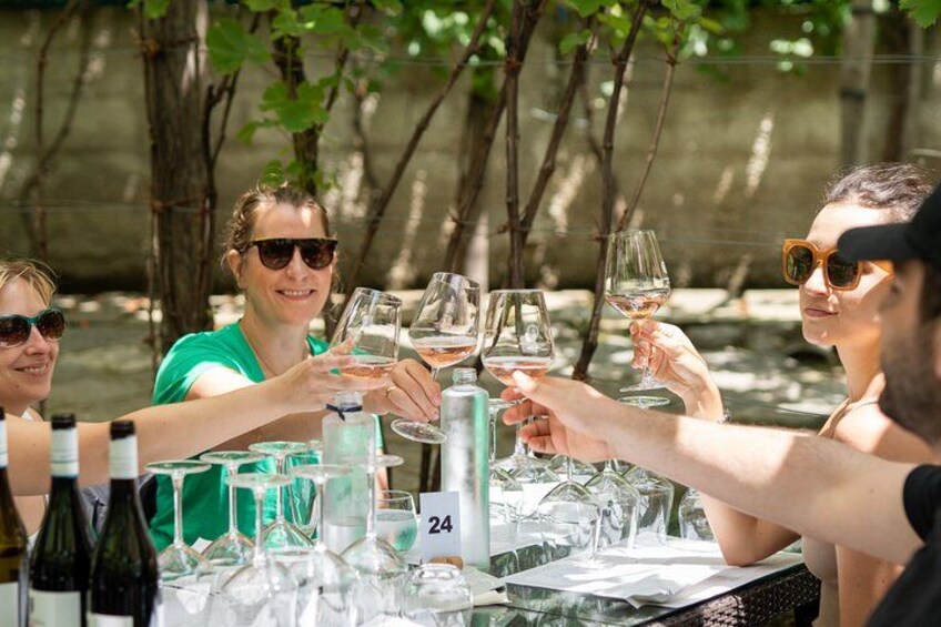 A group of people toasting with wine glasses at a table with bottles and glasses of wine. 1