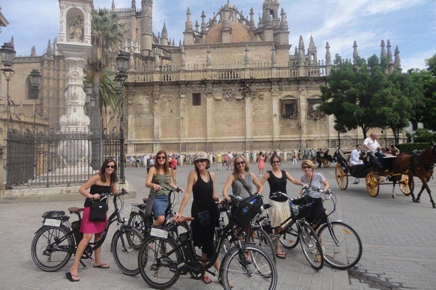 A group of people on bicycles in front of a historic building with a statue and a horse-drawn carriage in the background. 5