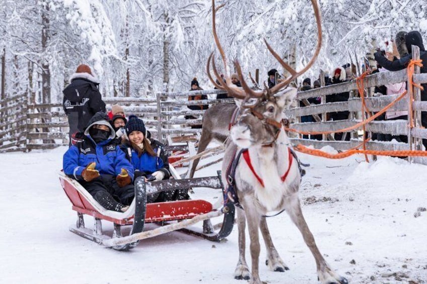 Ein Rentier zieht einen Schlitten mit Personen in Winterkleidung. 2