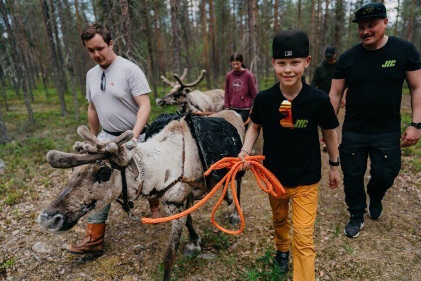 A person leading a reindeer with a rope, in a forested area. 1
