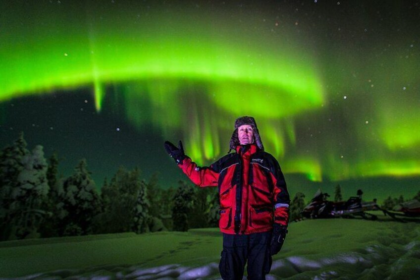 A person in a red jacket standing on snow with the aurora borealis in the background. 5