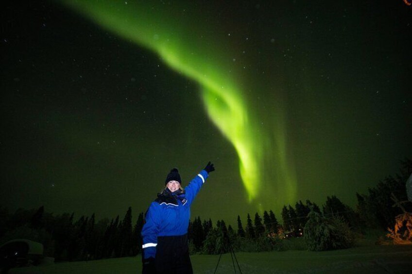 A person standing outdoors at night, pointing towards the sky where the aurora borealis is visible. 5