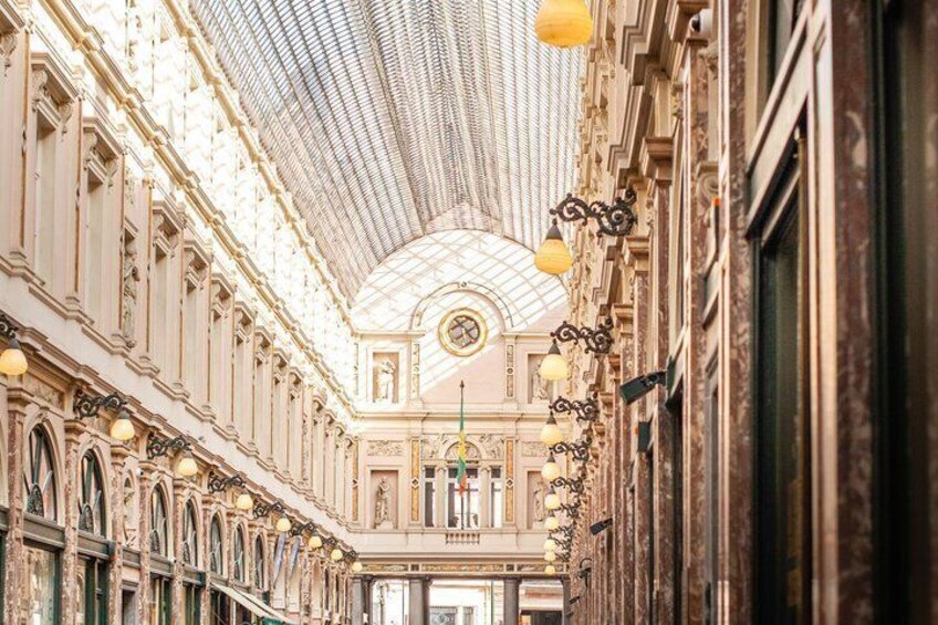 An ornate indoor corridor with a glass ceiling and classical architecture. 4