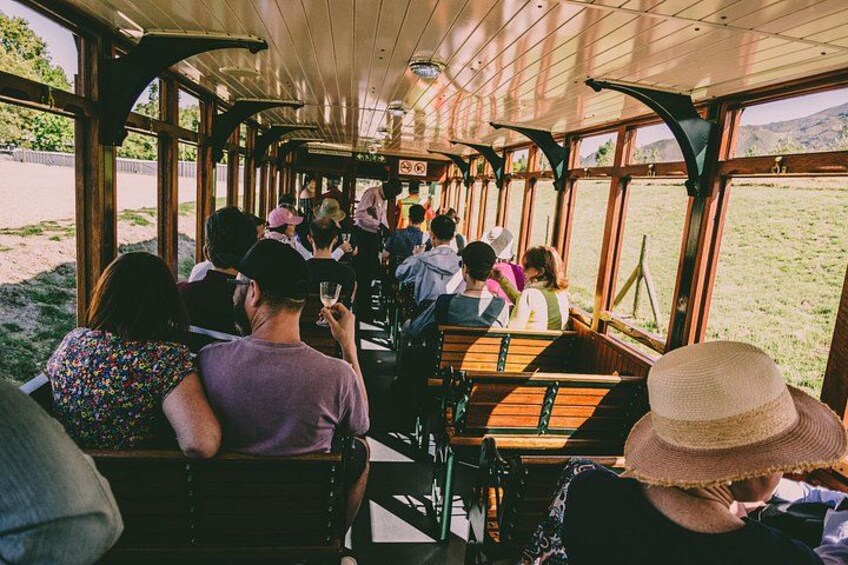 A group of people on a train with large windows, some holding drinks, and a grassy landscape outside. 2
