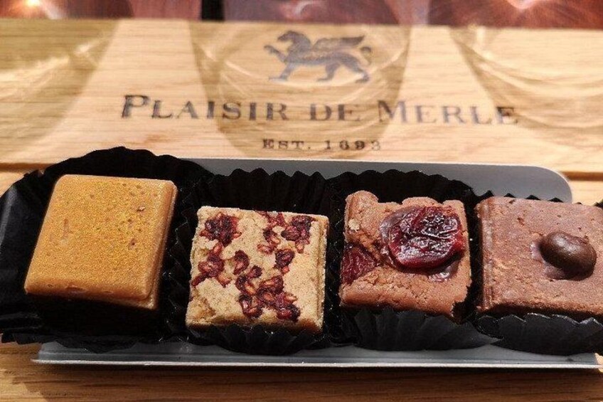 A tray of assorted chocolates on a wooden table with a placard reading 'Plaisir de Merle EST. 1893' in the background. 3