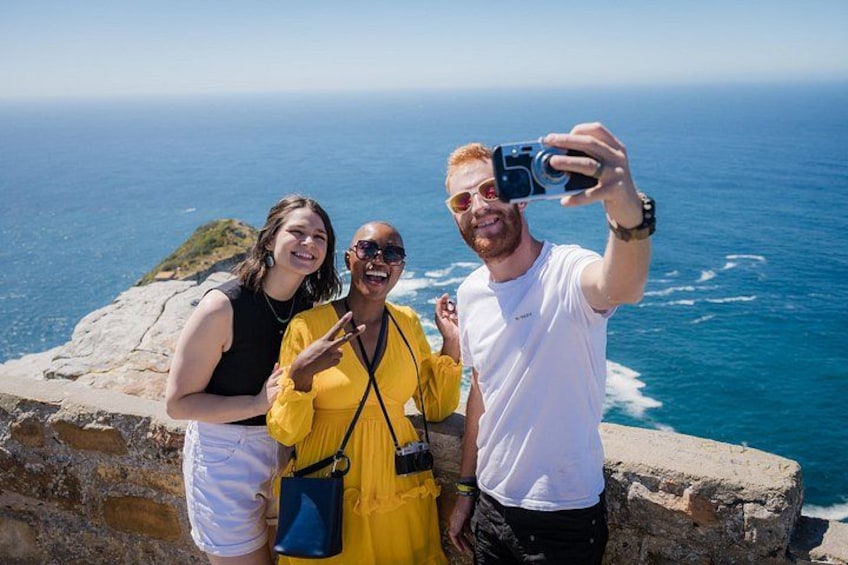 Three people taking a selfie on a rocky cliff overlooking the ocean. 3