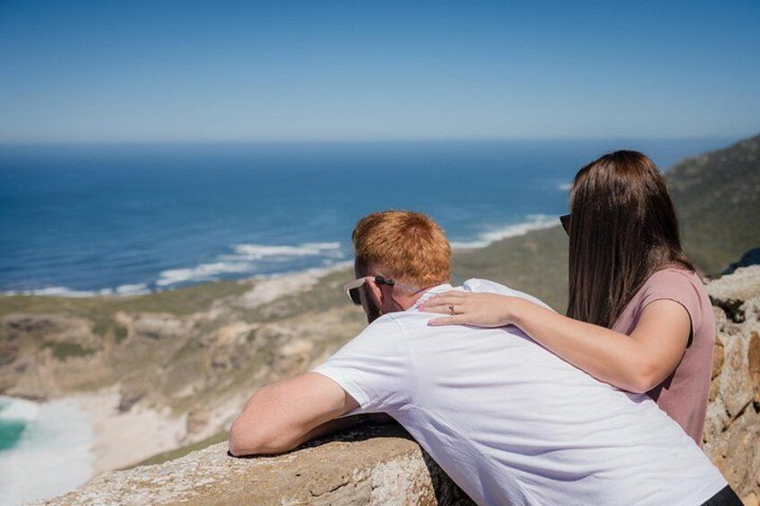 Una pareja abrazándose en un promontorio rocoso con vista al océano. 3