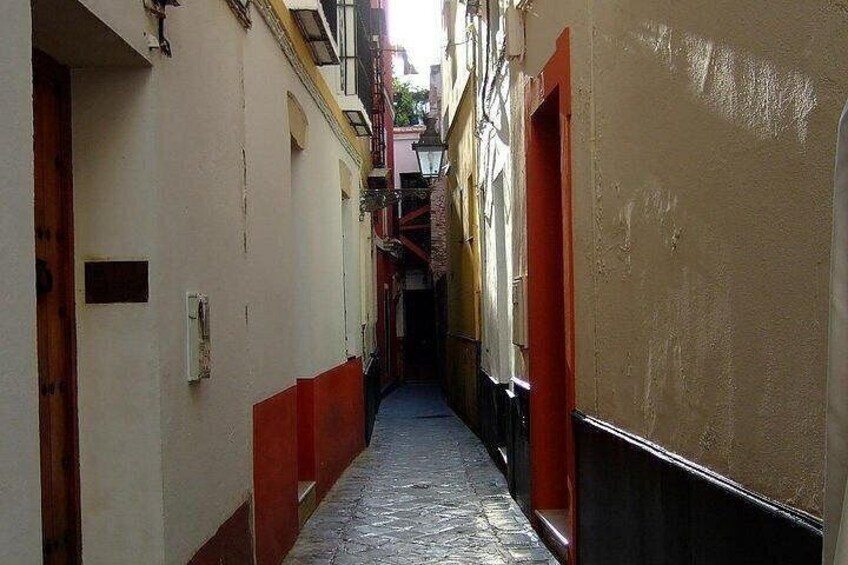 A narrow alleyway with buildings on either side, some with red doors and others with white walls. 2