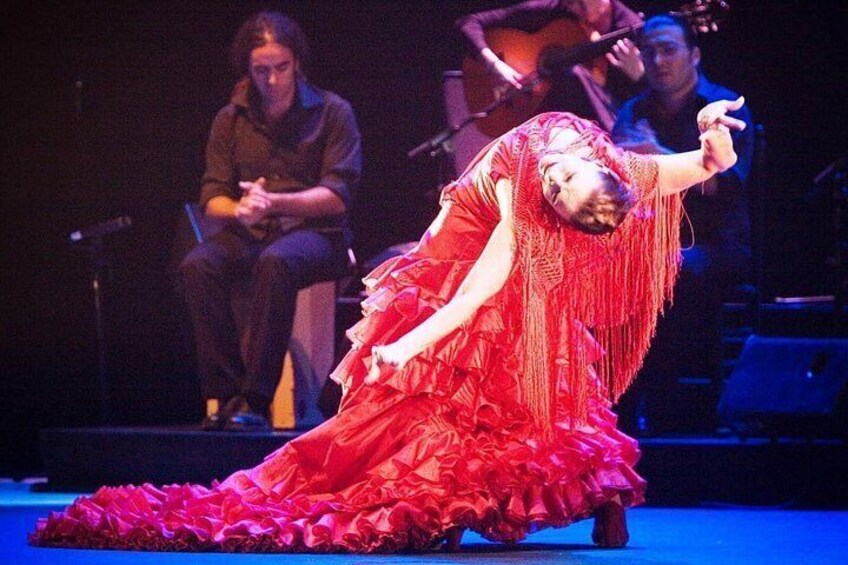 A person in a red dress with ruffles, performing on stage with a band in the background. 1