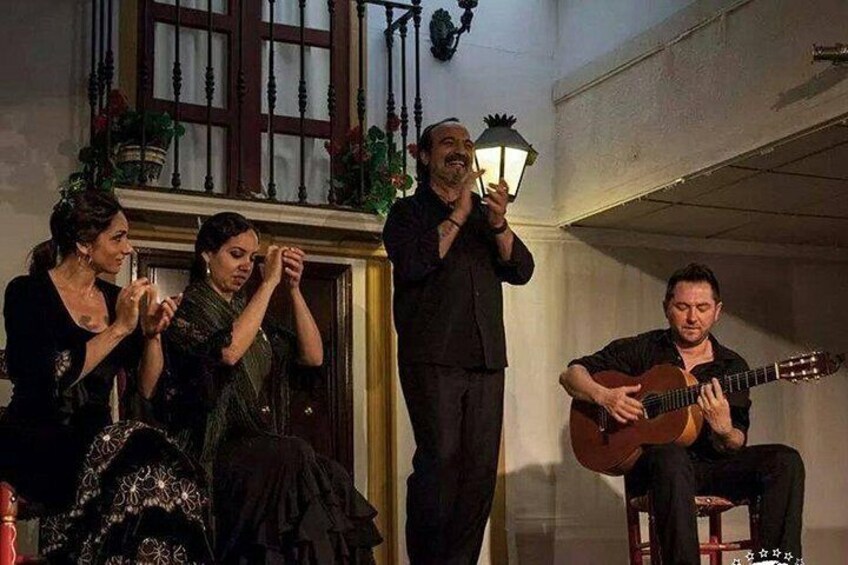 A group of people in a room with a piano, a guitar, and a person holding a lantern. 3