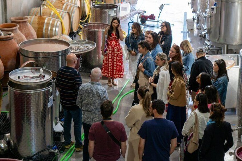 A group of people in a brewery with large stainless steel tanks and barrels. 2