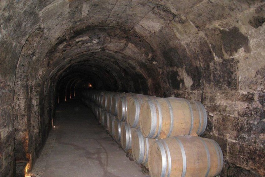 A stone tunnel with wooden barrels lined up on the right side. 3