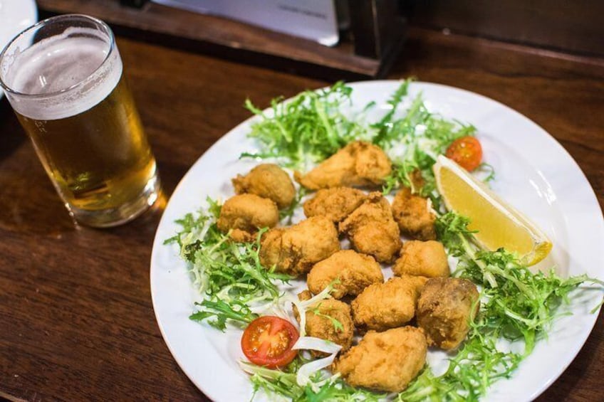 Eine Portion frittierter Hähnchennuggets mit einem Limettenschnitz und Kirschtomaten auf einem Bett aus Grünzeug, dazu ein Glas Bier. 4