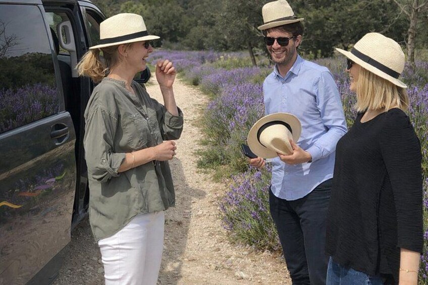 Three people standing by a vehicle in a field with purple flowers. 2