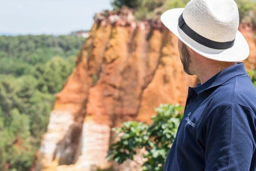 Una persona con camisa azul y sombrero blanco, de pie frente a una formación rocosa roja. 5